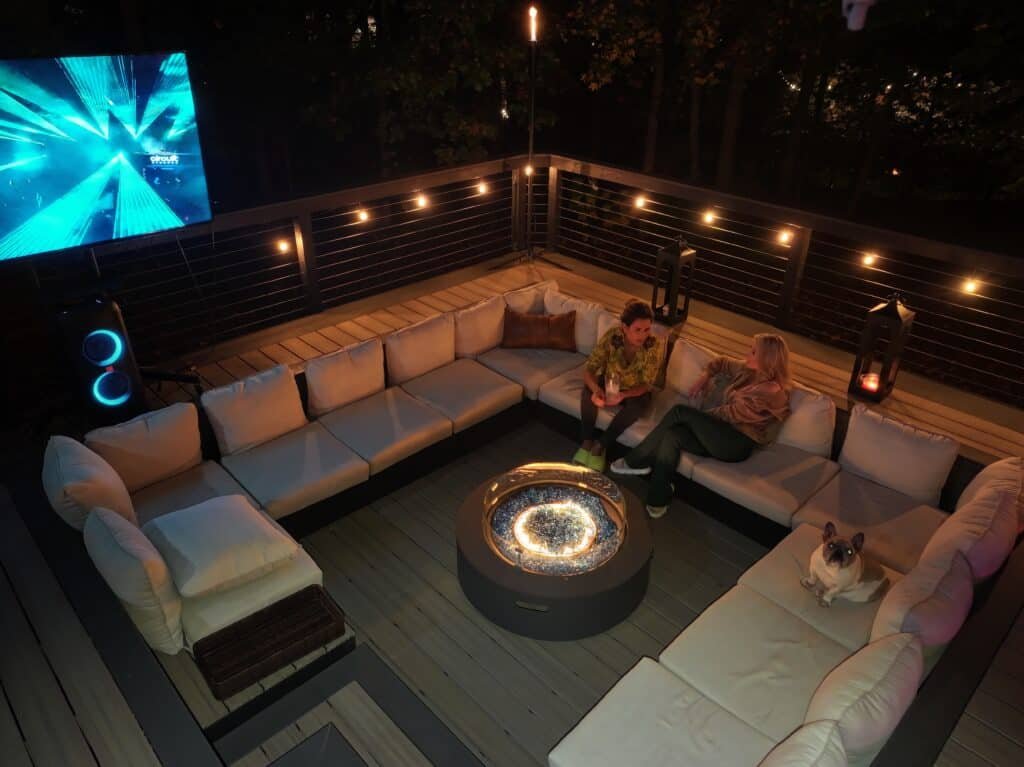 Cozy deck seating area at night with warm lights and a fire feature